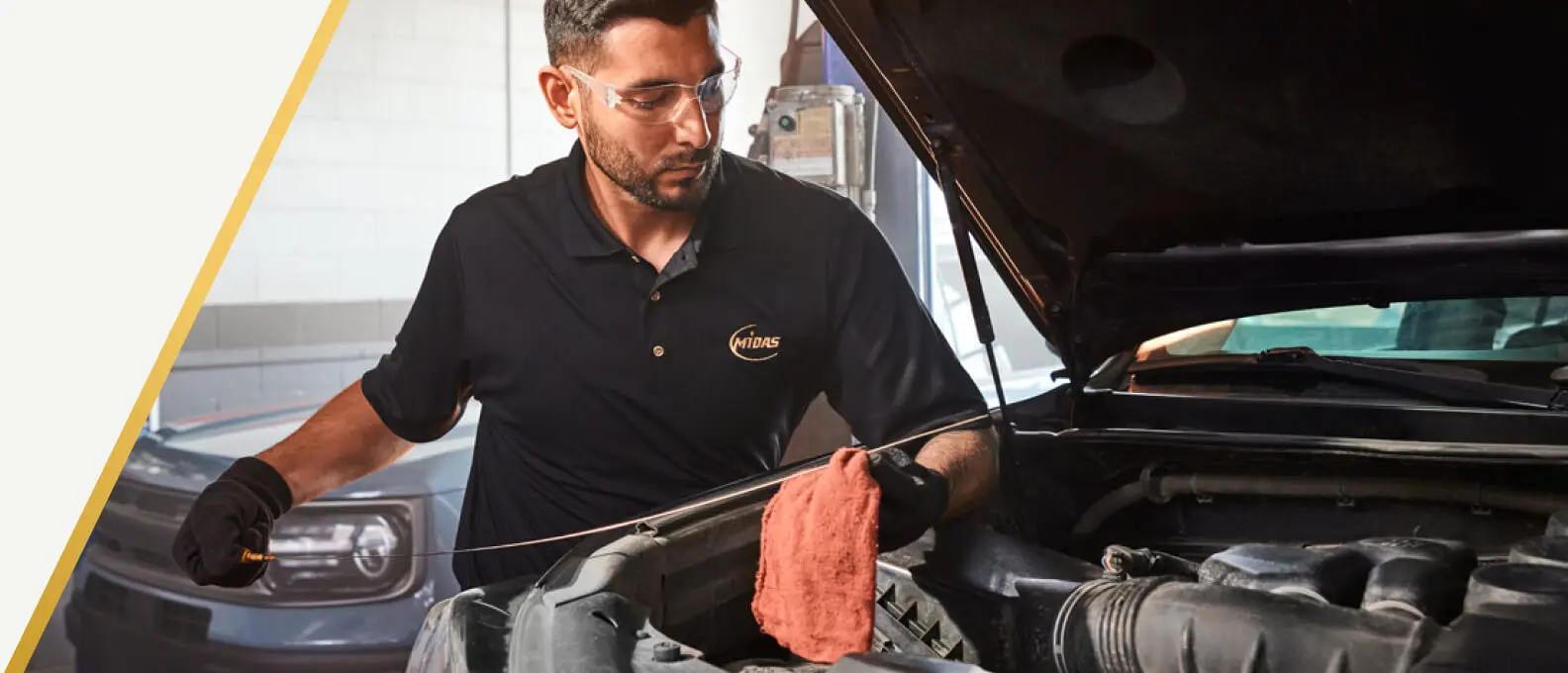 Midas technician checking the engine oil under the hood of a car